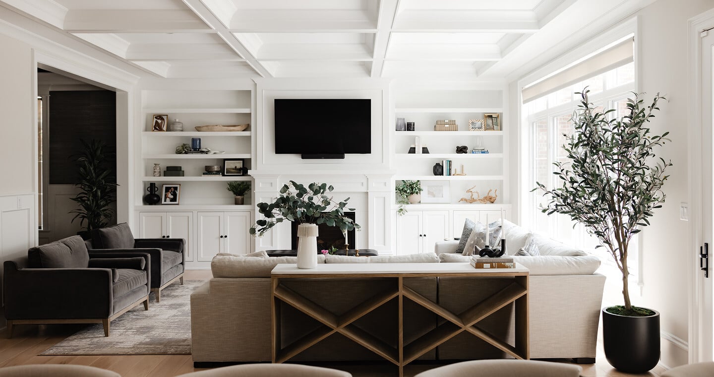 Living room in an Elmhurst, IL home with a coffered ceiling, white built-in shelving, linen sectional and a potted olive tree, designed by Dara Agruss Design