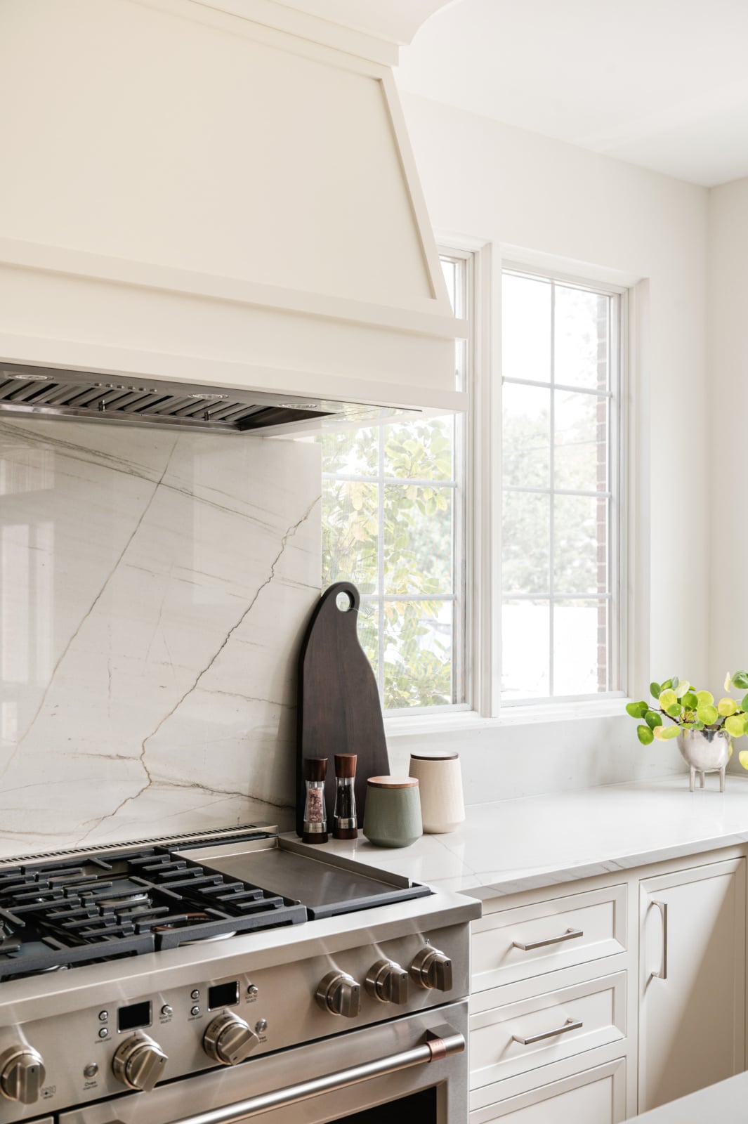 Range wall with a marble slab backsplash and custom hood in an Elmhurst, IL kitchen by Dara Agruss Design