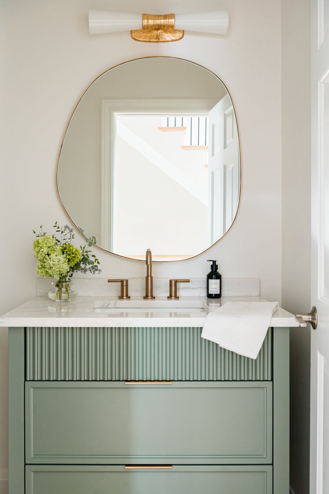 Powder room with a fluted sage green vanity, brass fittings and an organic mirror in an Elmhurst, IL home by Dara Agruss Design