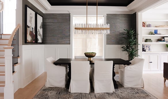 Modern dining room with a dark wooden table, six white slipcovered chairs, a crystal chandelier, abstract art, and built-in shelves with decor items.