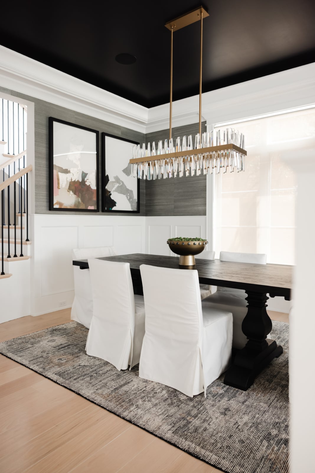 Dining room with a black painted ceiling, brass linear chandelier and slipcovered chairs in an Elmhurst, IL home