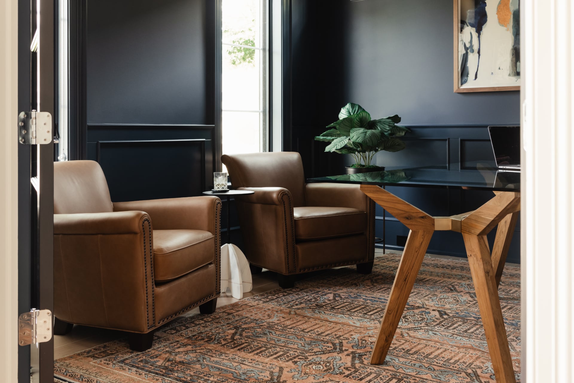 Navy panelled study with leather seating and a wood table in an Elmhurst, IL home by Dara Agruss Design