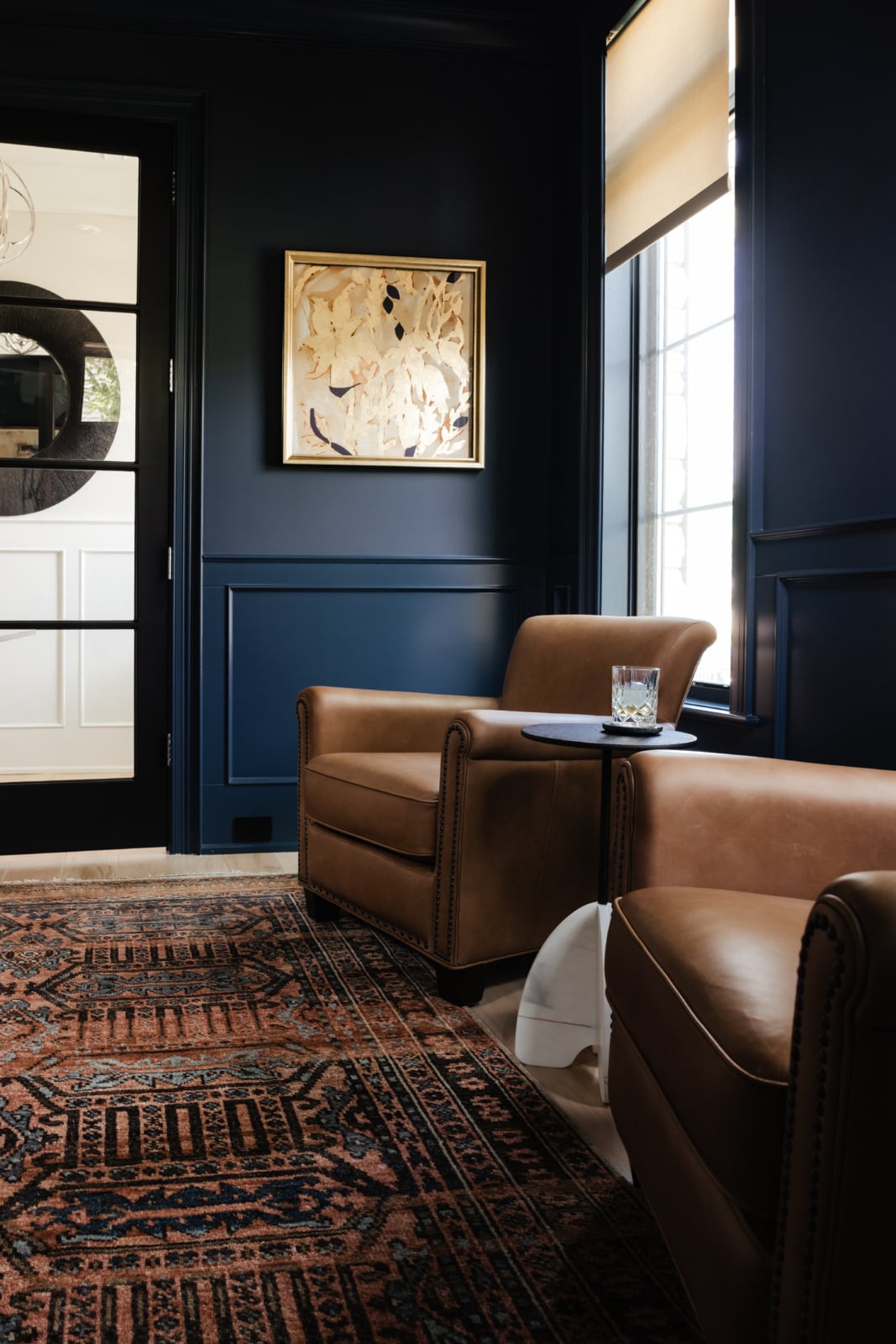 Leather club chairs and a patterned rug in a navy panelled study in an Elmhurst, IL home by Dara Agruss Design