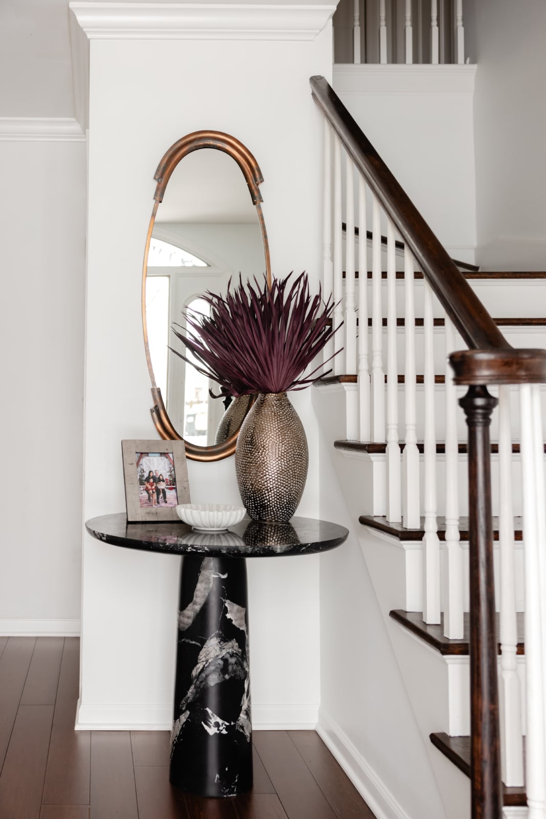 Entry hall with a dark staircase, round brass mirror and a marble console in an Oak Brook, IL home by Dara Agruss Design