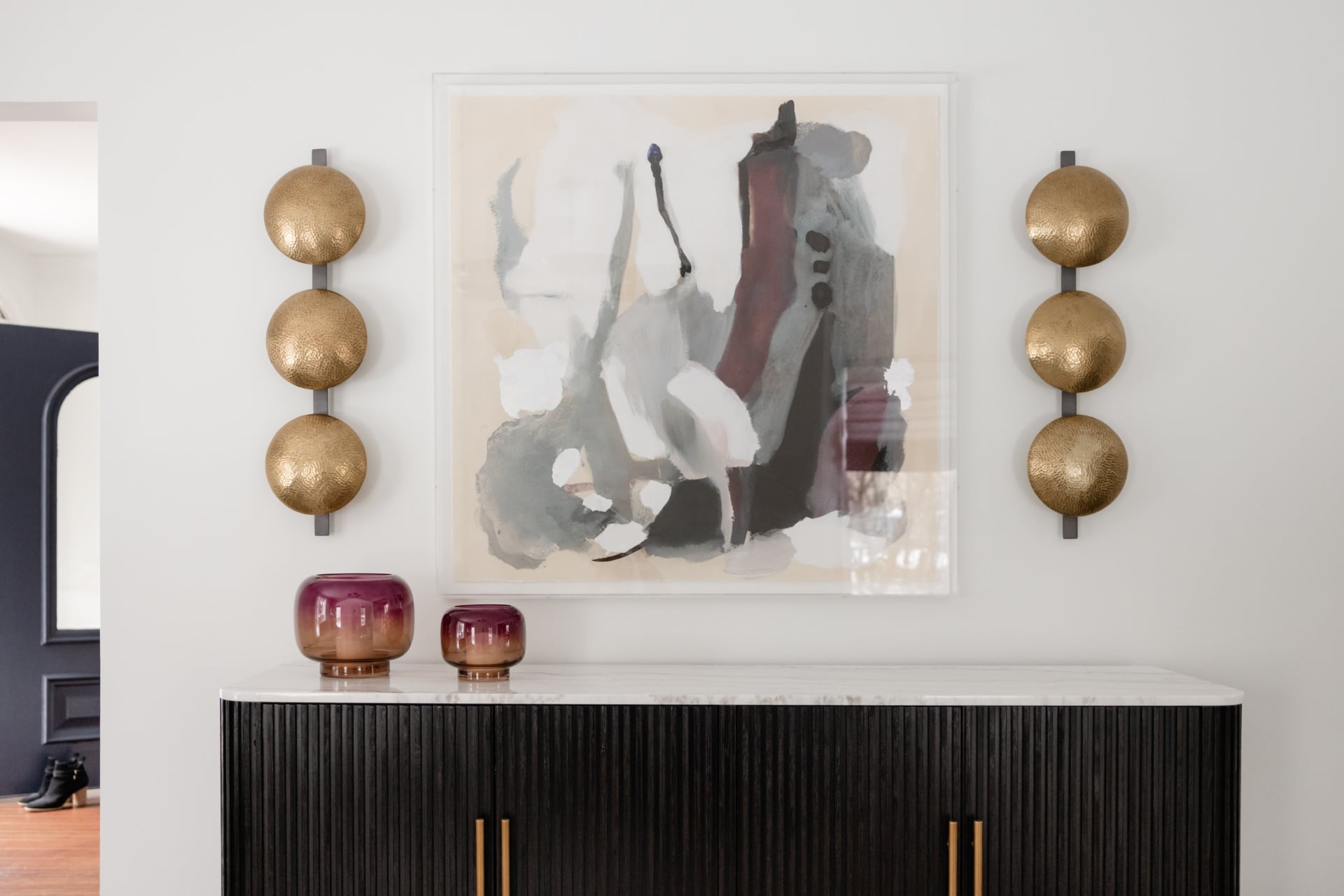 Fluted credenza with brass sconces and commissioned abstract art in an Oak Brook, IL home by Dara Agruss Design