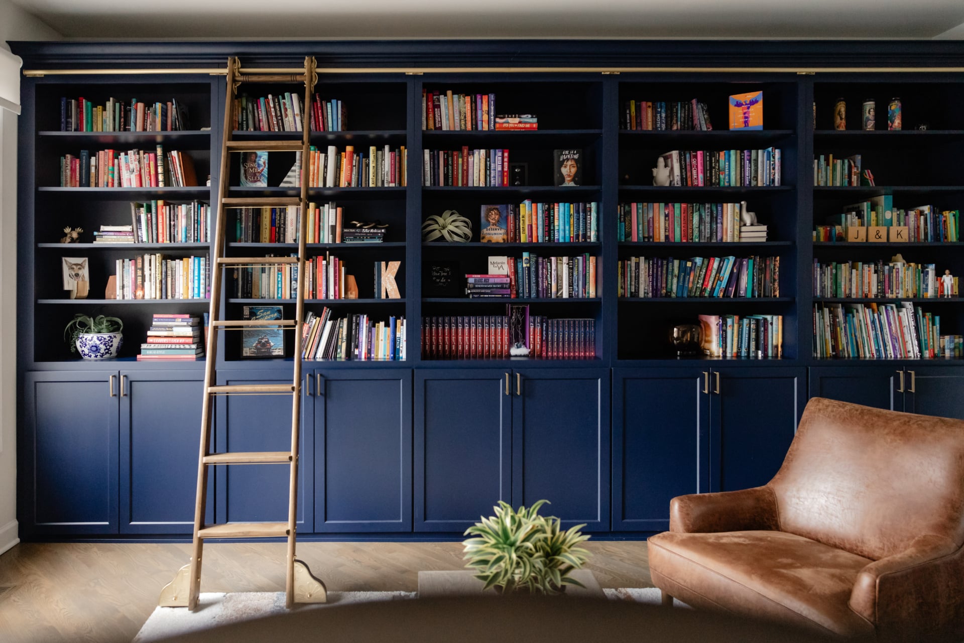 Navy home library with built-in shelving, a rolling ladder and leather seating, designed by Dara Agruss Design