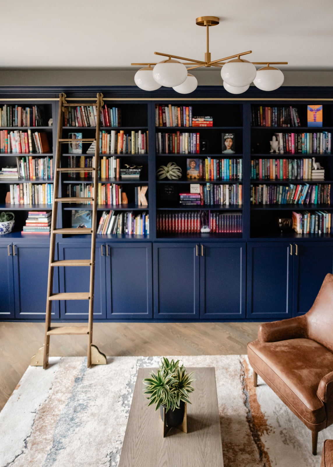 Home library panelled in deep navy with a brass rolling ladder and floor-to-ceiling shelving, designed by Dara Agruss Design