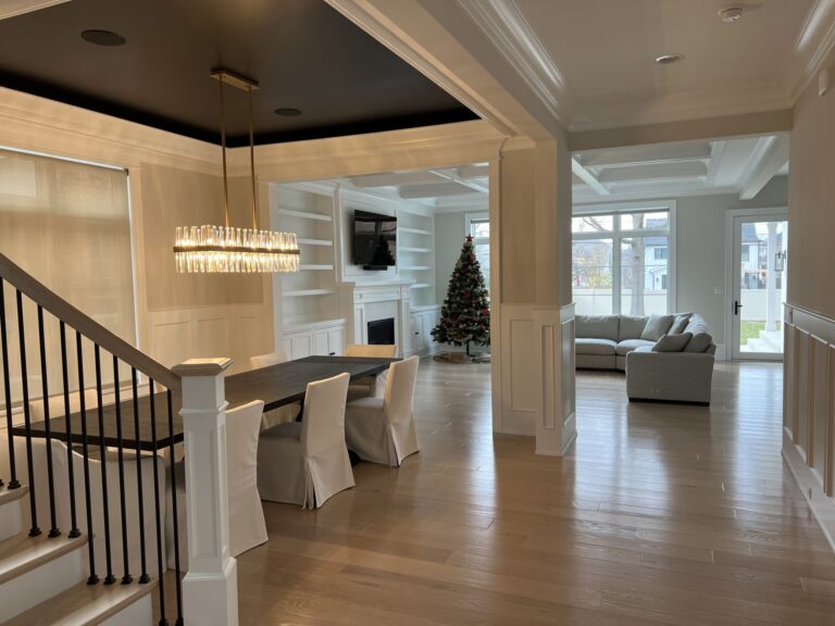 Modern open-concept living and dining area with a dark ceiling, chandelier, covered chairs, fireplace, TV, Christmas tree, large windows, and light wood floors.
