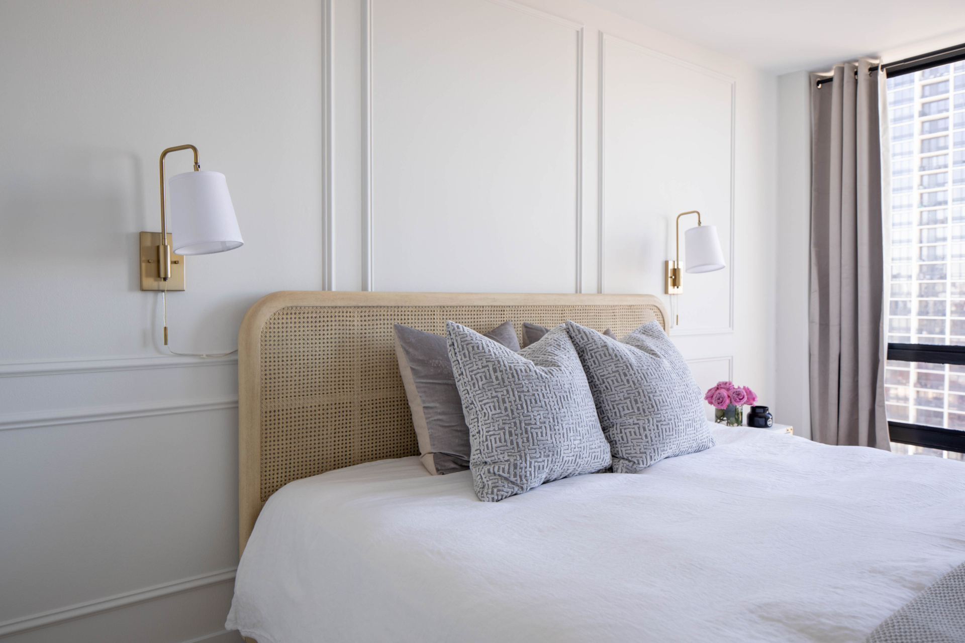 Bedroom with a cane headboard, blush walls and wall-mounted bedside lighting