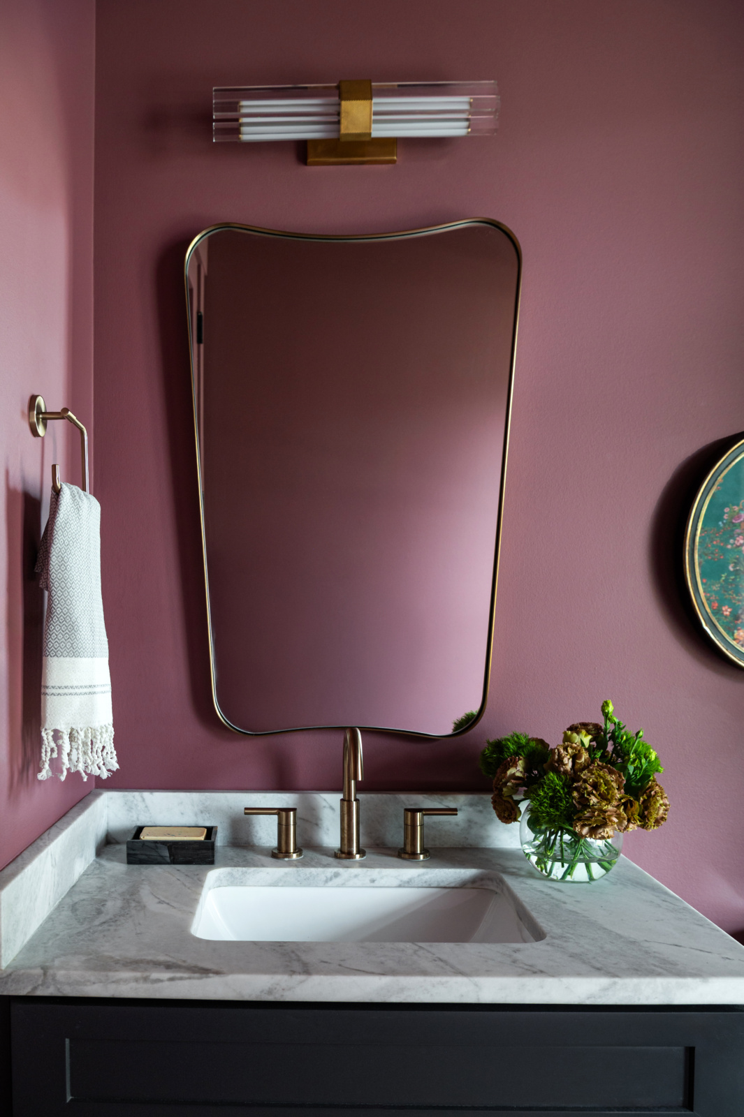 Powder room vanity with a sculpted brass mirror, marble top and mauve walls
