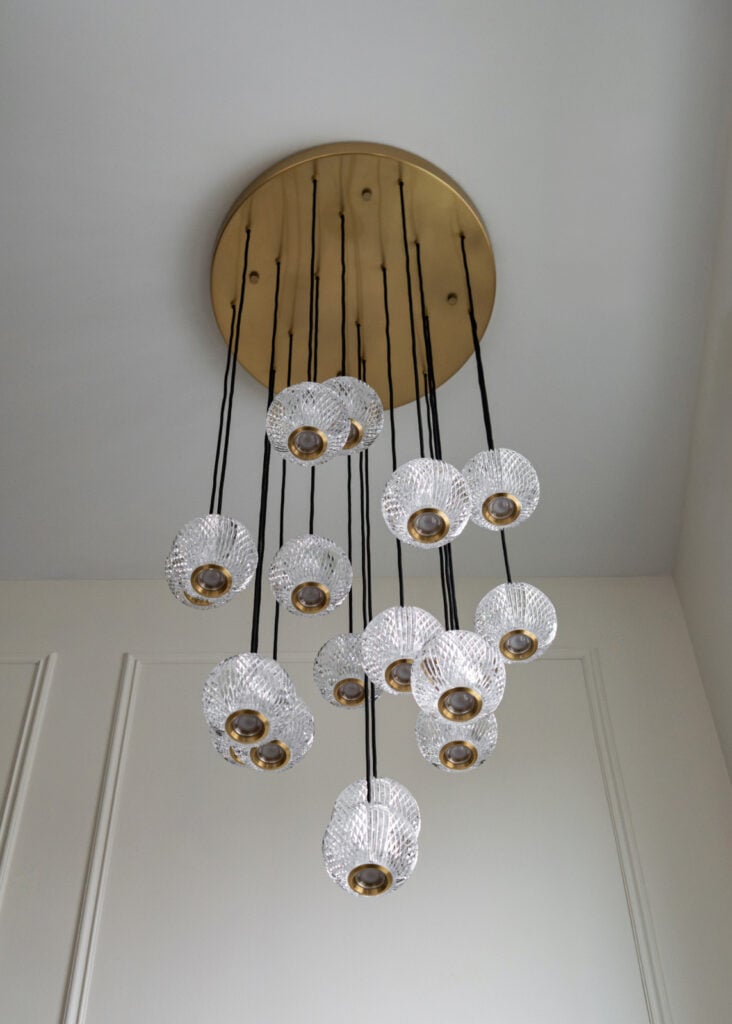 Large gold ceiling fixture with multiple glass pendant lights hanging at different heights on black cords.