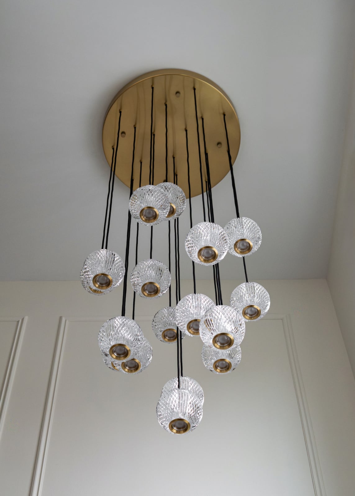 Large gold ceiling fixture with multiple glass pendant lights hanging at different heights on black cords.