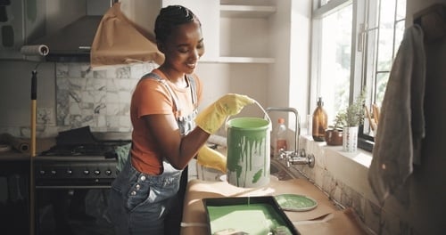 woman wearing rubber gloves pouring paint into tray during home remodeling