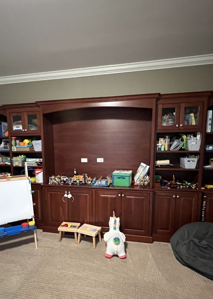 Playroom built-in cabinetry before renovation, stained dark cherry with a recessed arched alcove and beige carpet