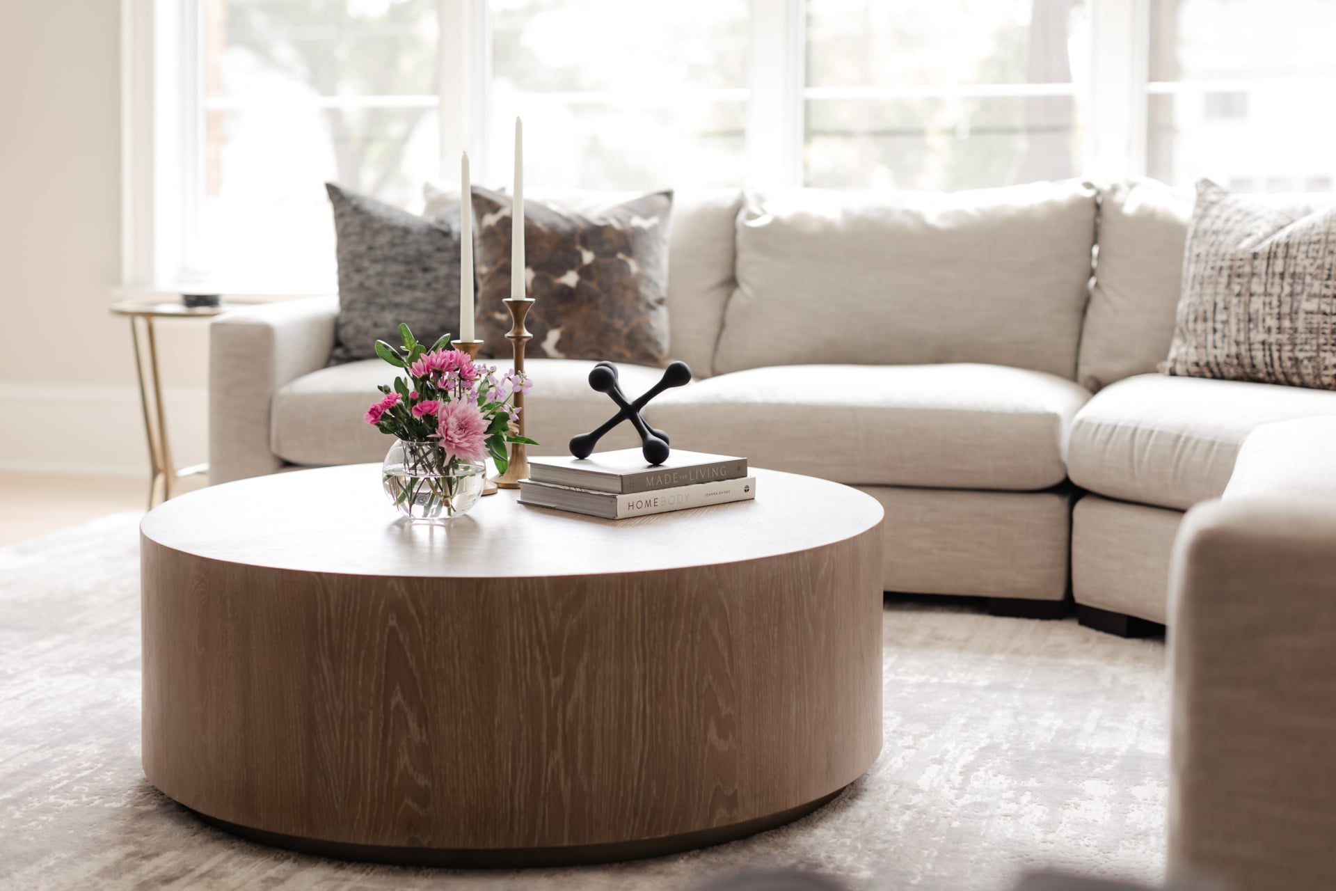 Round oak coffee table styled with books and flowers in front of a linen sectional