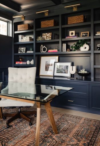 Office with wall-mounted dark blue bookshelves and glass desk