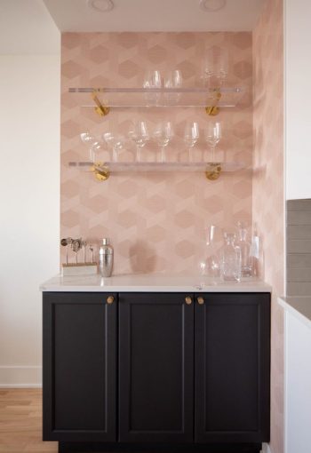 Bar area with light pink walls, black cabinets, and glass shelves