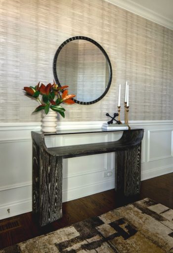 Entryway with dark accent table, round mirror, and textured wallpaper